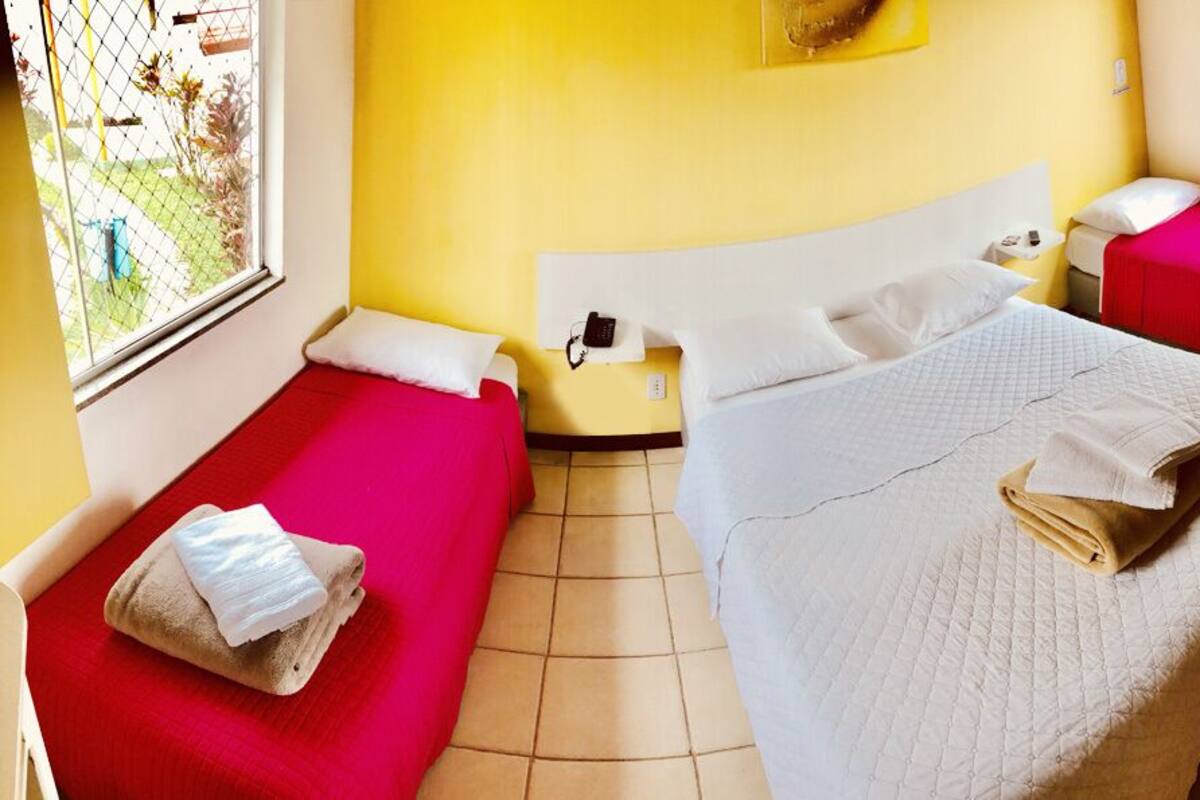 Habitación de hotel con dos camas individuales, una con cubrecolcha rojo y la otra con cubrecolcha blanco. Hay una mesita con un teléfono y una lámpara entre las camas.
