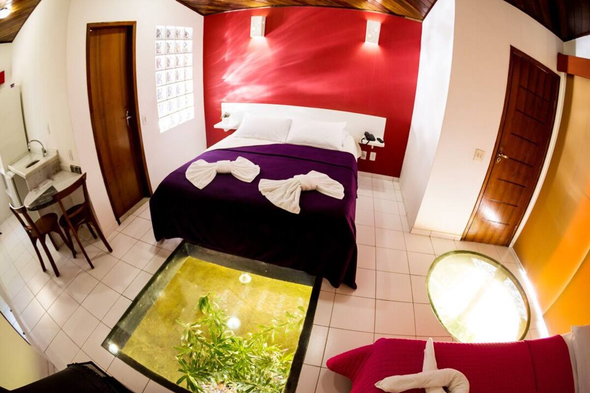 Habitación de hotel con cama, una mesita con una planta, un sofá rojo y un espejo.