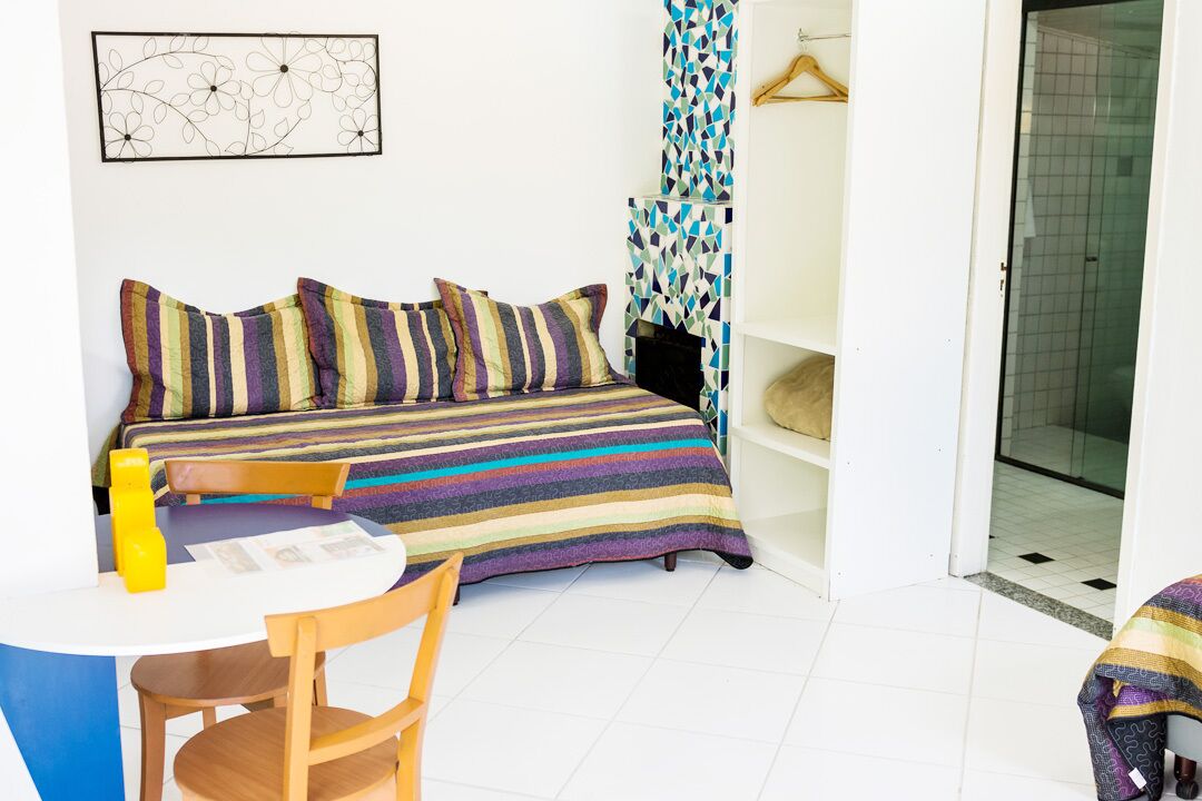 Una habitación pequeña e iluminada con una cama, una mesa y una silla. Hay una puerta que da a un baño.