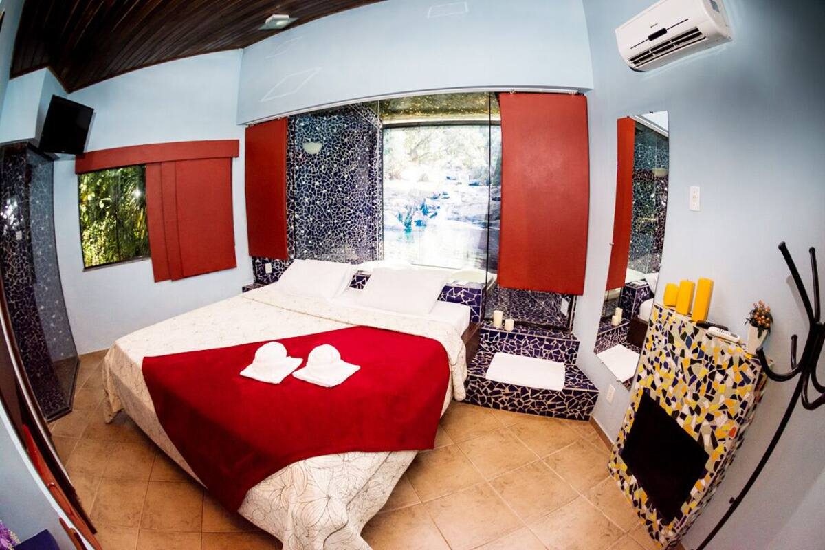 Un dormitorio con cama, ventana, espejo y una mesita de noche con artículos de aseo.