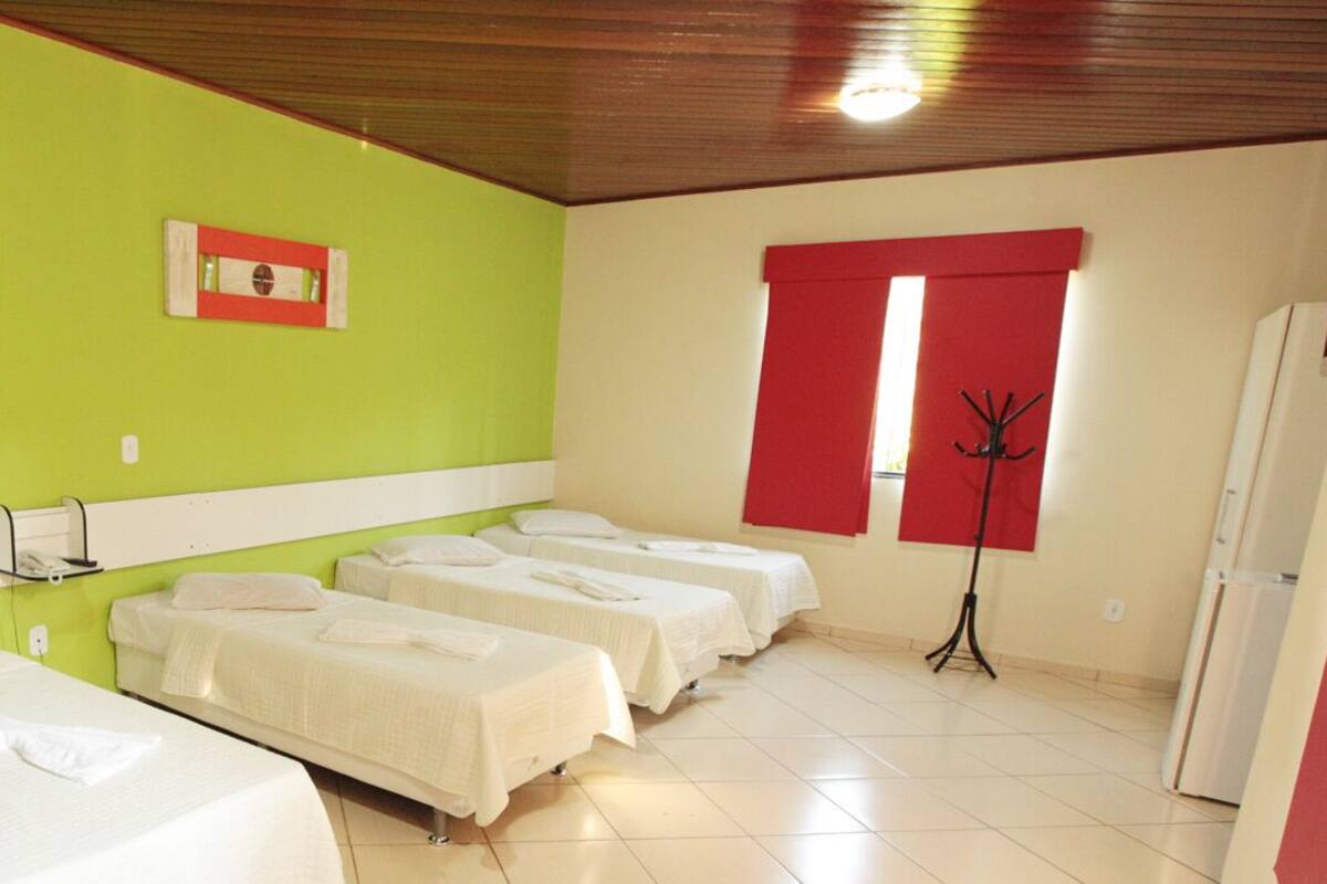 Habitación de hotel con cuatro camas individuales, un perchero, una cortina roja y un ventanal pequeño.