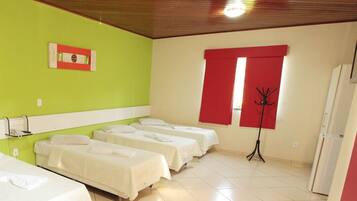 A hotel room with four single beds, a coat rack, a red curtain, and a small window.
