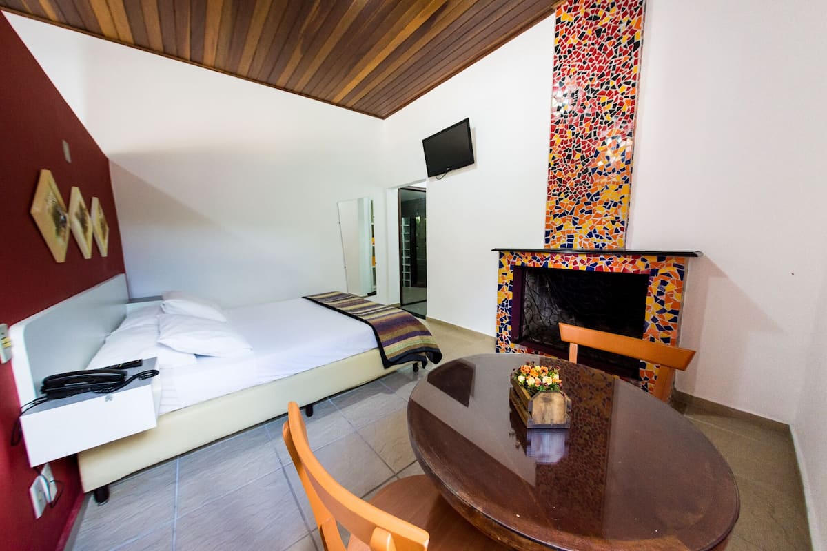 Un dormitorio con una cama, un televisor montado en la pared, una mesita con un jarrón de flores y un llamativo muro de mosaicos.