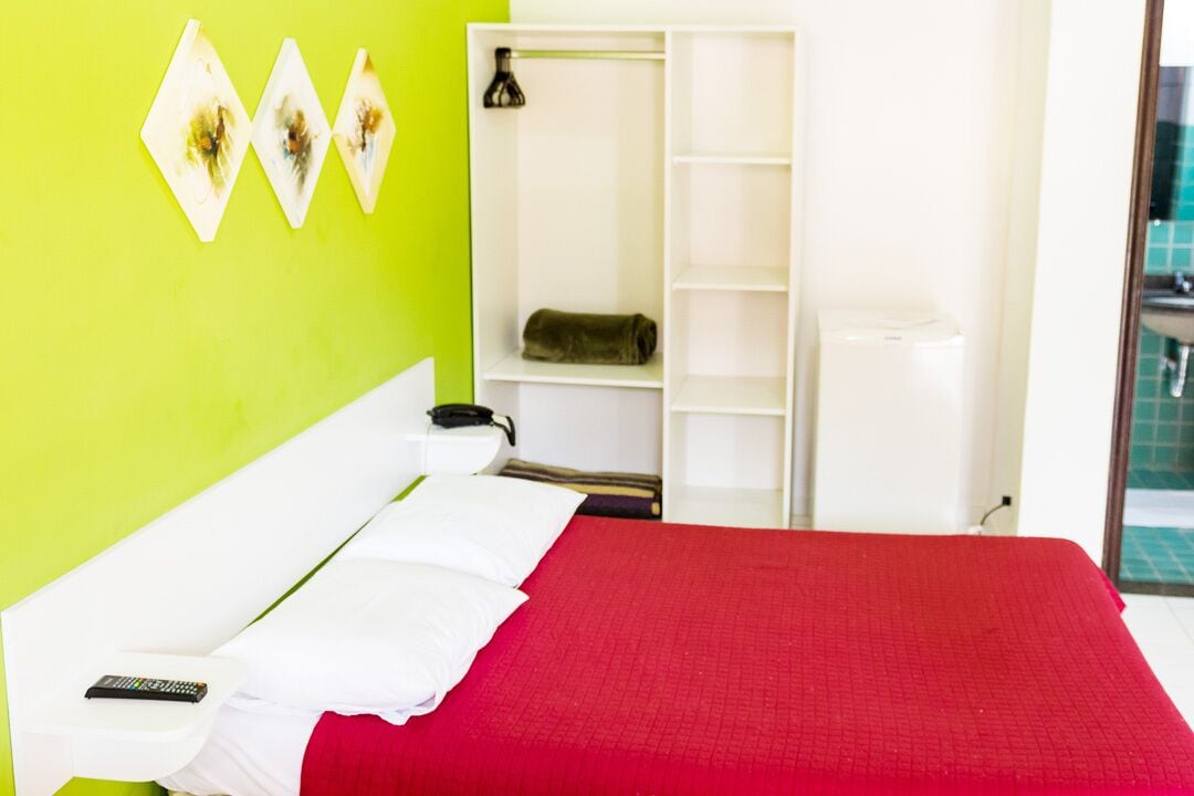 Habitación de hotel con una cama, un armario blanco y una pared verde.