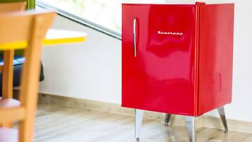 A red cabinet with a handle, standing on metal legs, in a room with a wooden chair and a yellow table.