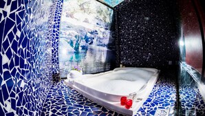 A modern bathroom with a mosaic blue and white tiled wall, a white bathtub, and a small shelf with two red candles. - Pousada Suarez (Itatiaia)
