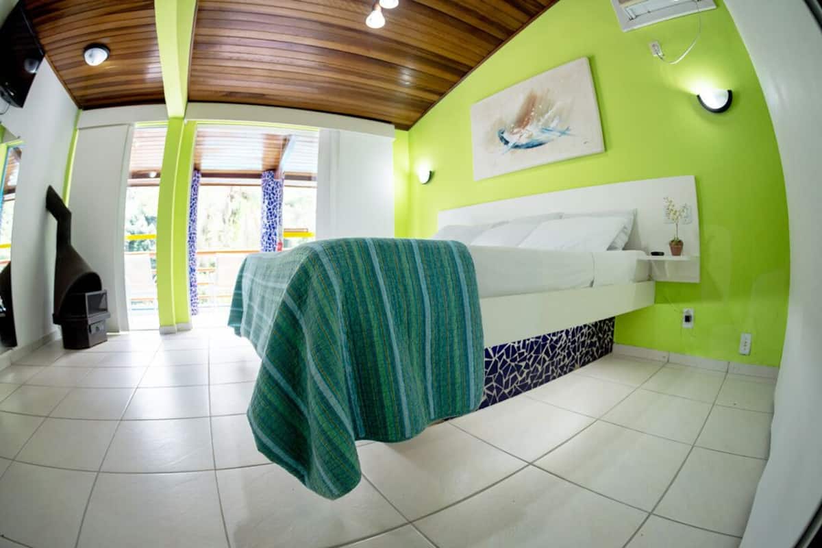 Un dormitorio con cama, mesita de noche, lámpara de pared y ventana con cortinas.