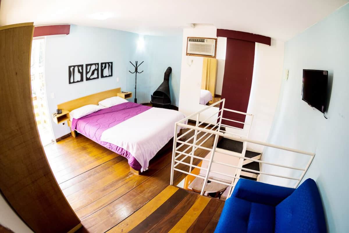 Un dormitorio con cama, una silla, perchero y televisor.
