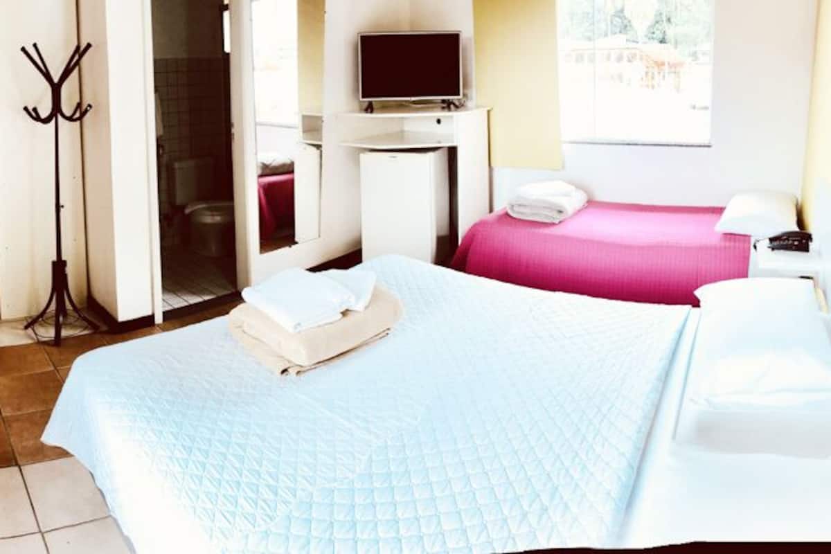 Habitación de hotel con una cama grande, un escritorio con televisor y un baño visible a través de una puerta abierta.