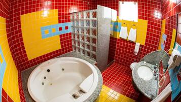 Casa de banho com parede revestida a azulejos vermelhos e amarelos, uma banheira branca, uma pia com espelho e um porta-toalhas.