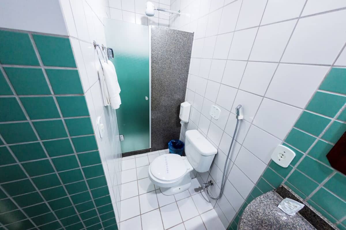Un baño con un inodoro blanco, ducha y pared con azulejos verdes.