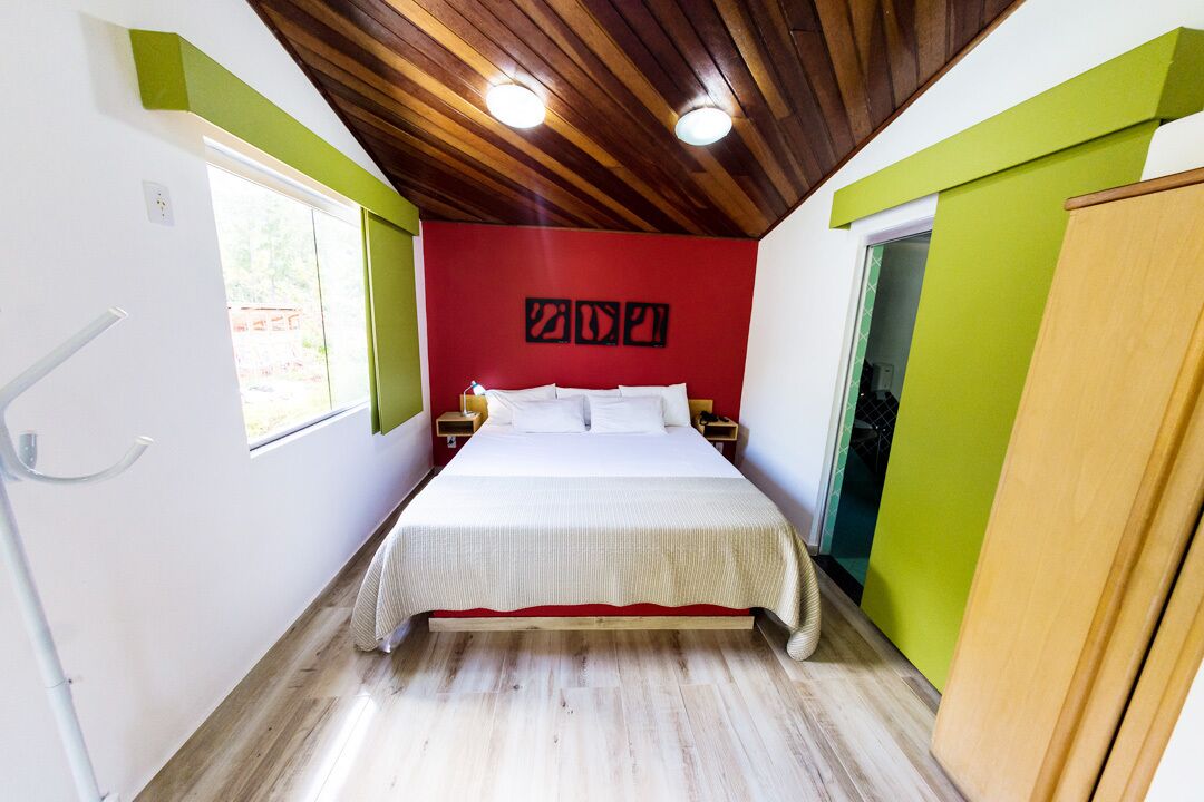 A bedroom with a bed, a wooden ceiling, a red accent wall, and a green accent wall.