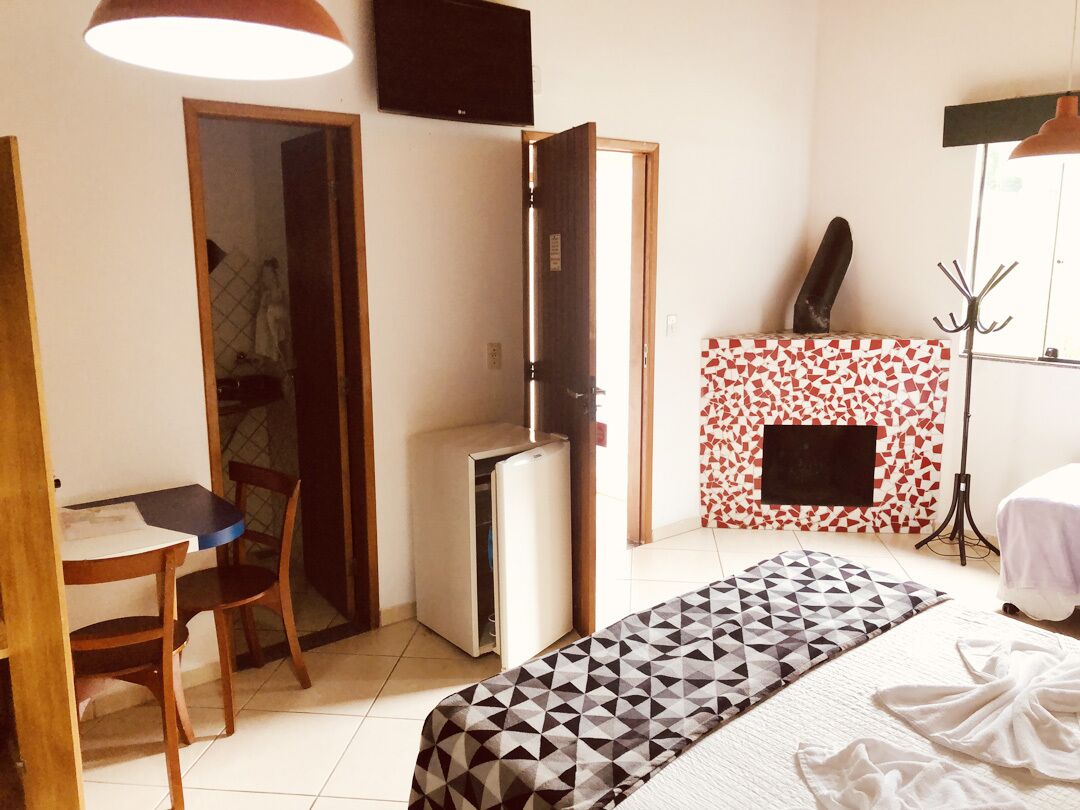 Um quarto com uma cama, uma escrivaninha, uma cadeira, um guarda-roupa, uma televisão e uma lareira.
