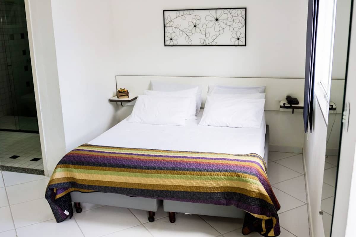 Una cama bien hecha con una manta colorida a rayas, una mesita de noche con una lámpara y una obra de arte en la pared sobre la cama.