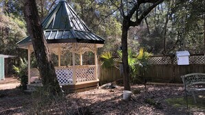 Un kiosque doté d’un toit en treillis, entouré d’arbres et d’une clôture en bois.
