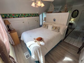 A bedroom with a large bed, a ceiling fan, a wall-mounted shelf with decorative items, and a window with curtains. - Minutes from the beach, with indoor hot tub (Daufuskie Island)