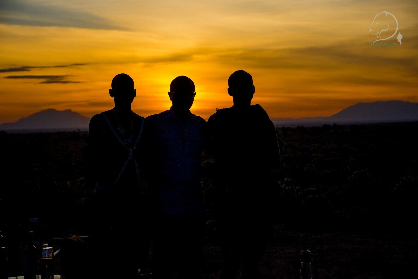 Three silhouetted figures against a sunset with mountains in the background.