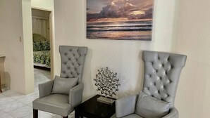 Una stanza con due poltrone grigie, un piccolo tavolo nero con una scultura metallica, e un grande quadro raffigurante un tramonto sull'oceano appeso al muro.