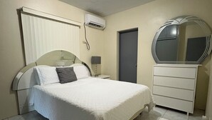 Una camera da letto con un letto, una cassettiera, uno specchio, un condizionatore e una porta.