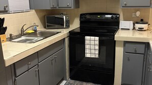 Una cucina compatta con mobili grigi, un piano cottura nero, un forno a microonde e un tostapane.