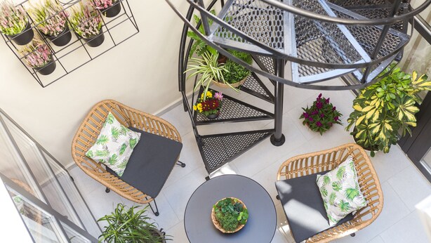 En balkon med fletmøbler, plantekrukker og en spiraltrappe.