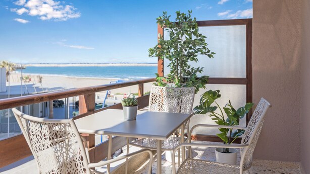 Un balcon avec une table et des chaises, donnant sur une plage et l’océan.