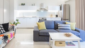 Un salon moderne avec un canapé gris, une table basse blanche et un coin cuisine à l’arrière-plan.