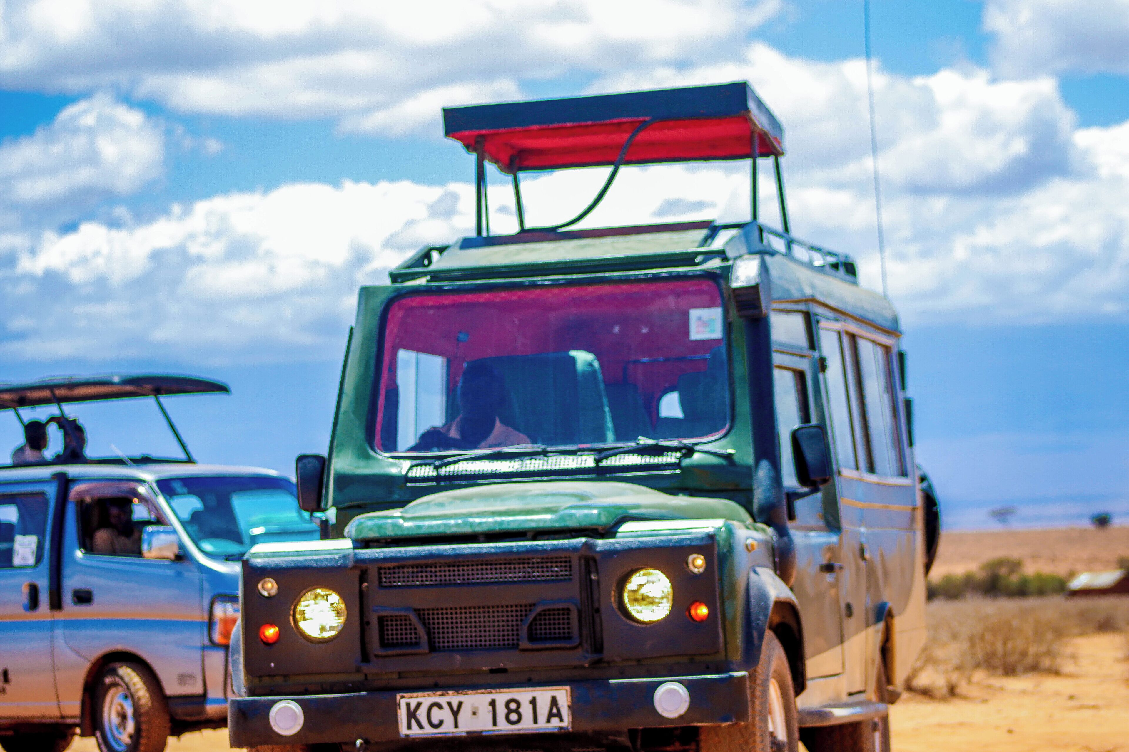 A green off-road vehicle with a red roof rack and a license plate reading "KCY 181A" parked in a desert-like environment.