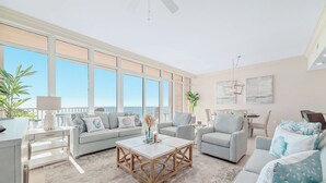 Ein geräumiges Wohnzimmer mit großem Fenster zum Meer, einem Holztisch und einer Sitzecke mit einer Couch und Sesseln.