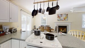 A kitchen with a white stove, hanging pots, a fireplace, and a dining area with chairs and a table. - River View House (Center Conway)