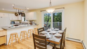 A modern kitchen with white cabinets, a granite countertop, and a dining area with wooden chairs and a table set for four. - River View House (Center Conway)