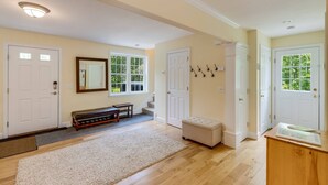 A spacious hallway with hardwood floors, white doors, and a bench. - River View House (Center Conway)