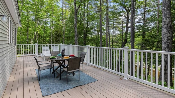 A wooden deck with a table and chairs, surrounded by a white railing, overlooking a forested area. - River View House (Center Conway)