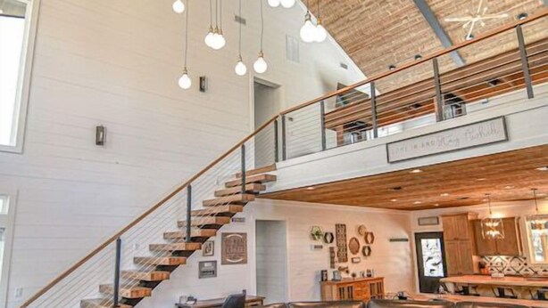 A spacious living area with a large sectional sofa, a wooden coffee table, and a staircase leading to an upper level. - Chasing Rainbows Lodge - 6 King Suites (Broken Bow)