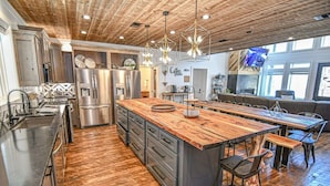 A modern kitchen with a large island, stainless steel appliances, and a wooden ceiling. - Chasing Rainbows Lodge - 6 King Suites (Broken Bow)