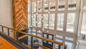 A spacious interior with a wooden herringbone wall, a staircase with a metal railing, and multiple windows allowing natural light. - Chasing Rainbows Lodge - 6 King Suites (Broken Bow)