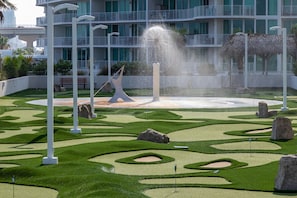 A landscaped garden with a fountain, white columns, and a building with balconies in the background.