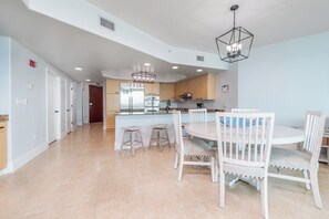 A modern kitchen with a central island, white dining chairs, and a hanging light fixture.