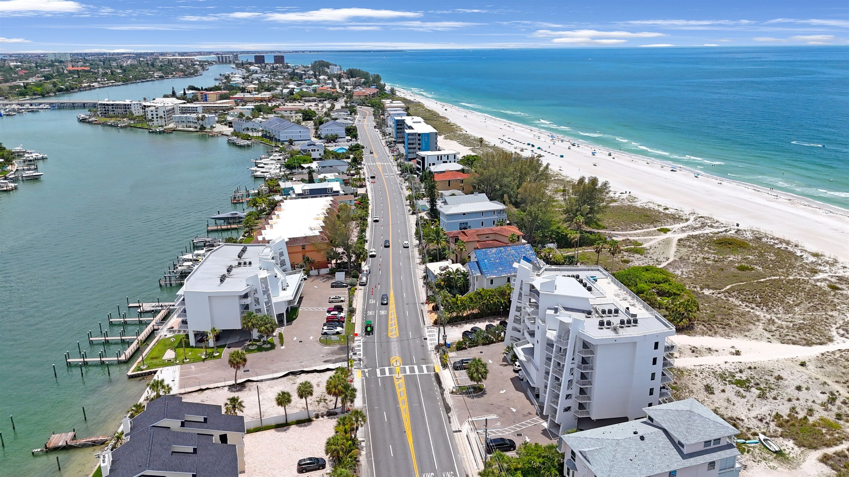 A coastal cityscape with a marina, beachfront, and modern buildings along the road.