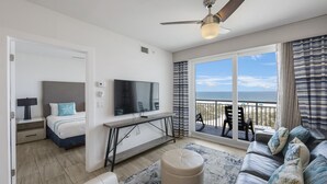 Une chambre d’hôtel moderne, dotée d’un lit, d’une télévision, d’un balcon avec vue sur la mer et d’un canapé en cuir.