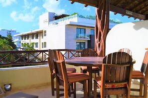 A terrace with wooden furniture and a view of a modern building with balconies. - La Olas By Riviera Rentals (Playa del Carmen)