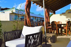 An outdoor seating area with wooden furniture, a white cushioned bench, and a table with chairs. - La Olas By Riviera Rentals (Playa del Carmen)