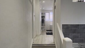 A narrow hallway leading to a bathroom with a toilet and a shower area.