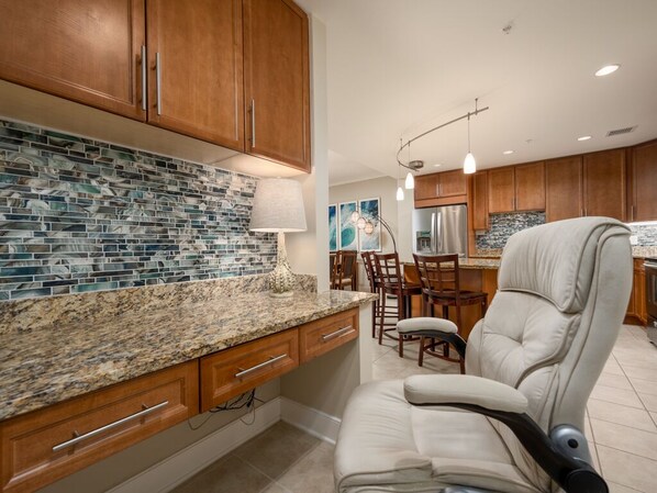A kitchen with wooden cabinets, a granite countertop, and a built-in seating area with a cushioned chair. - Beautiful furnishings throughout in this luxury condo on the ocean (Ocean City)