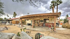 Un patio techado al aire libre con mobiliario, zona de barbacoa y vistas a un paisaje desértico con rocas y cactus.