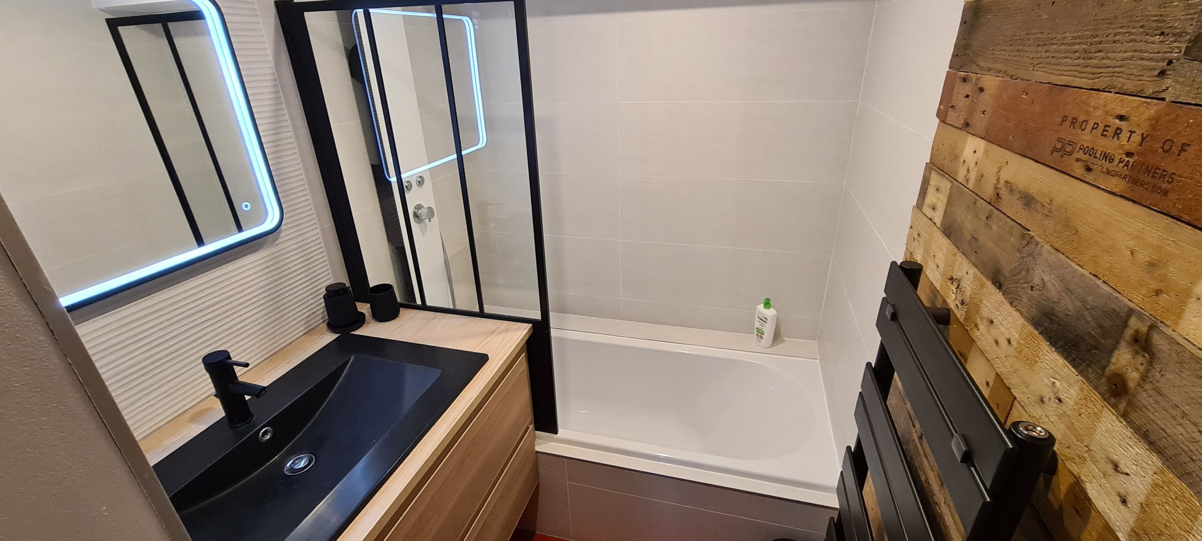 A modern bathroom with a glass shower enclosure, a wooden vanity with a black sink, and a wooden wall panel.