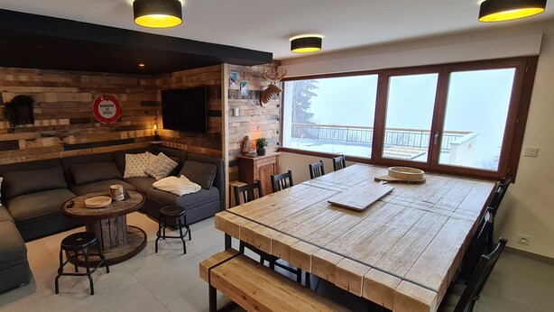 Un salon chaleureux avec un mur en bois, un canapé, une table basse et une table à manger avec des bancs.