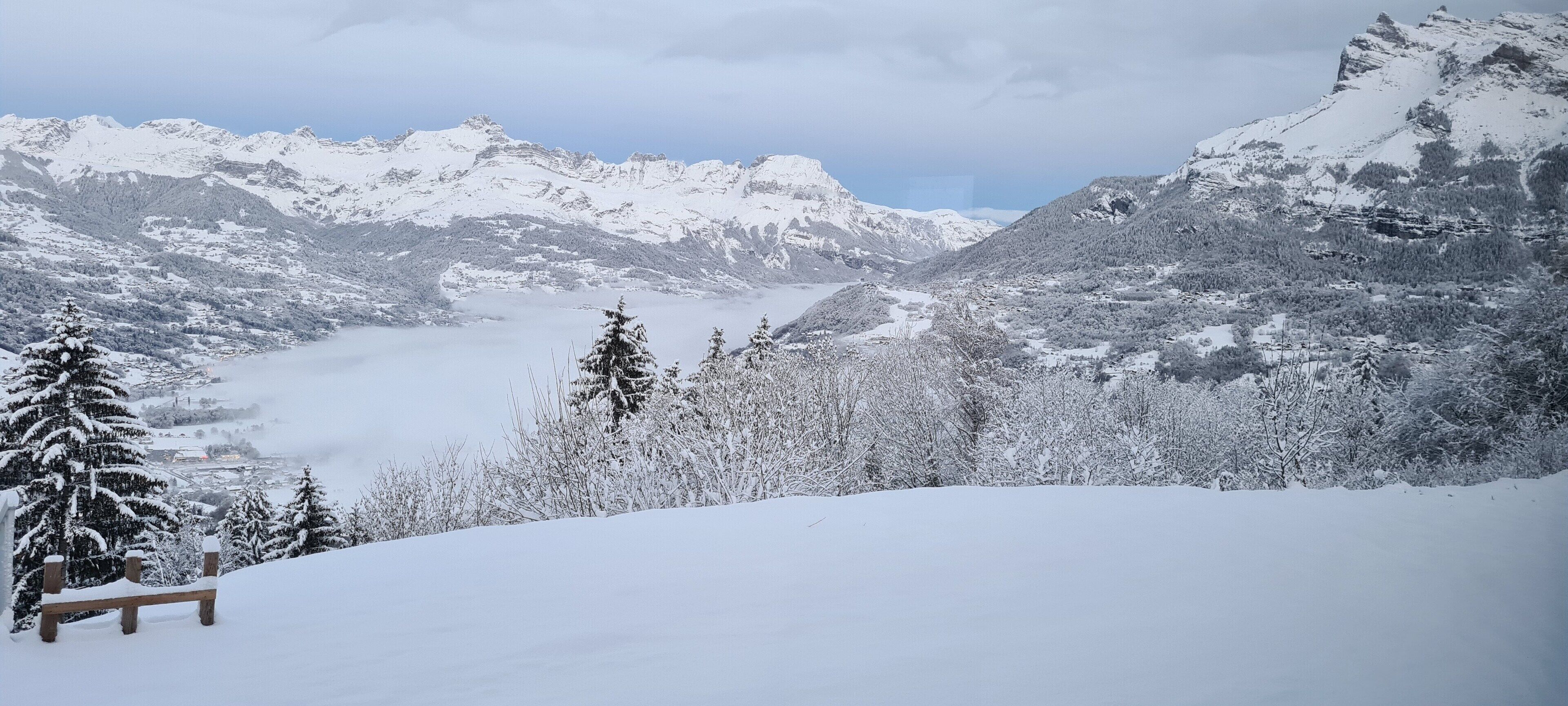 A snow-covered mountain landscape with a bench and trees.