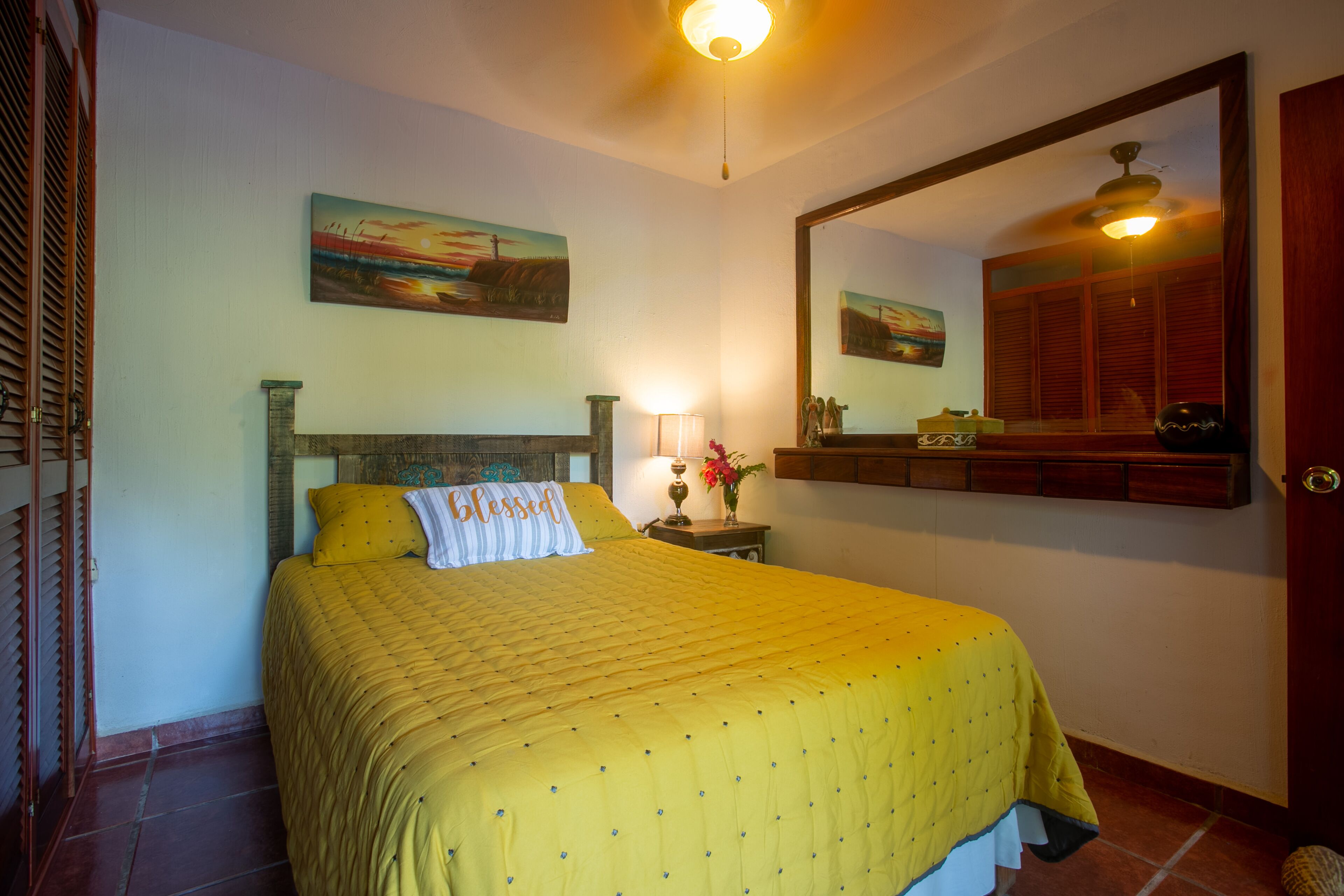 Una cama bien hecha con una colcha amarilla y una almohada con la palabra 'Blessed'.