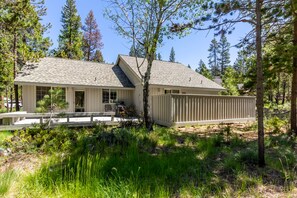 A two-story house with a covered porch and a fenced backyard, surrounded by tall trees and dense vegetation.